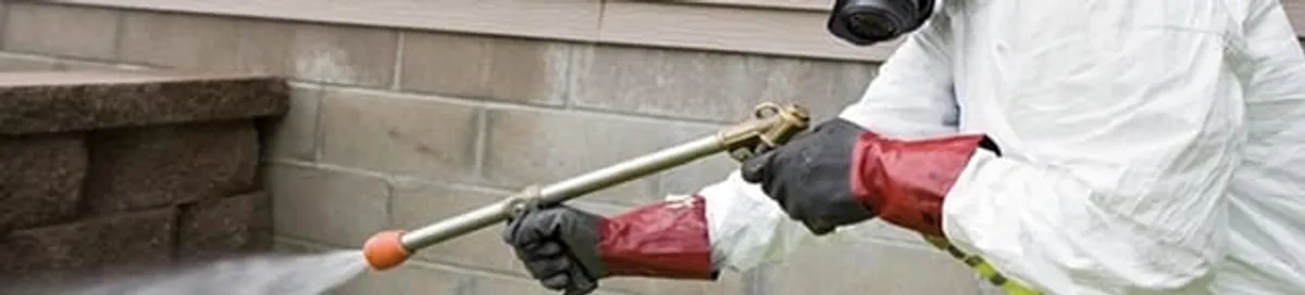 Pest control technician applying exterior insect treatment along a home foundation in Baton Rouge, LA