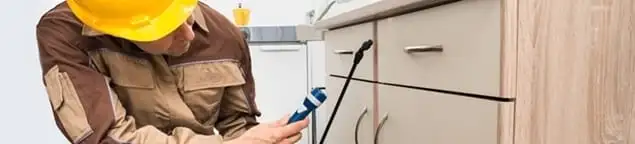 Roach exterminator applying treatment under kitchen cabinets in Baton Rouge, LA