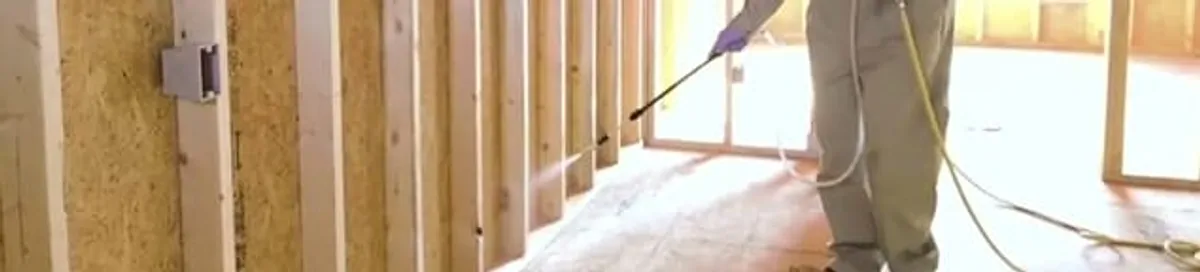 Termite treatment technician applying spray along framing and unfinished walls in Baton Rouge, LA