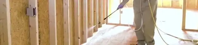 Termite treatment technician applying spray along framing and unfinished walls in Baton Rouge, LA